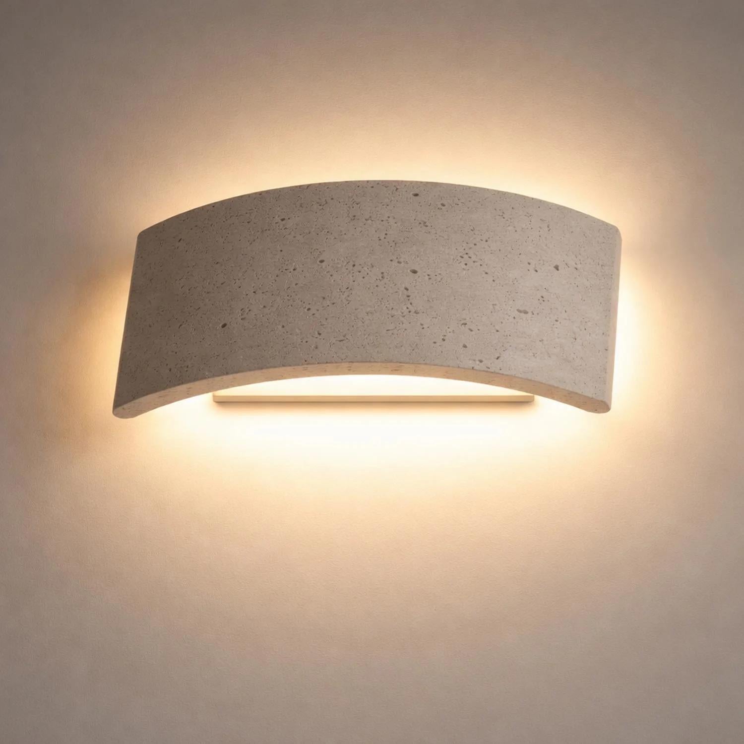 Curved travertine up/down wall light casting warm illumination on a light wall.