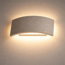 Curved travertine up/down wall light casting warm illumination on a light wall.