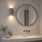 Black sandstone up/down wall light, cylindrical, casting light on a modern bathroom wall above a mirror.