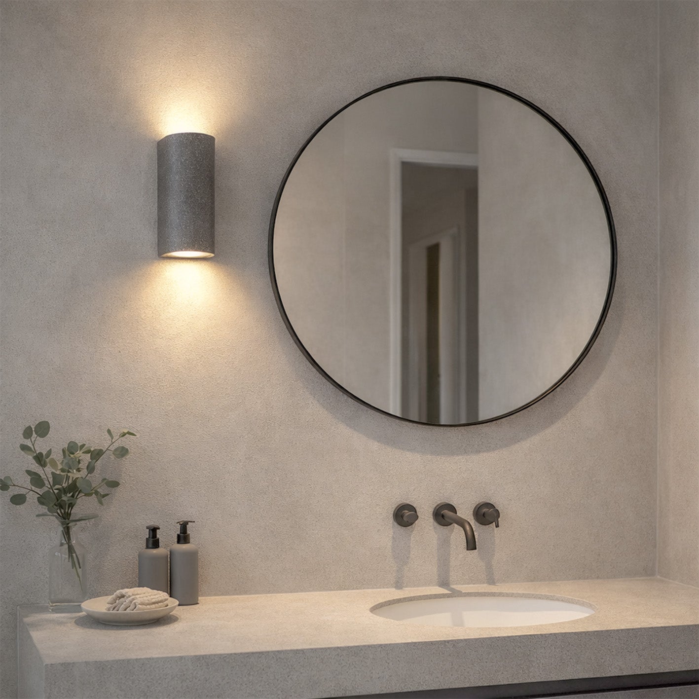 Black sandstone up/down wall light, cylindrical, casting light on a modern bathroom wall above a mirror.