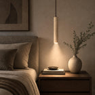 Slender natural travertine pendant light with downward glow, walnut cord, above a bedside table.