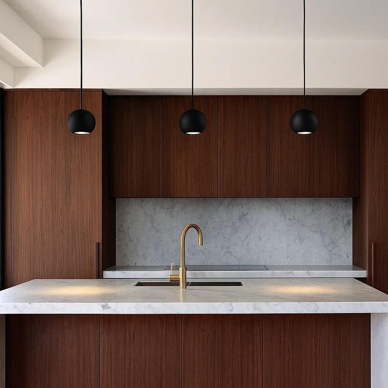 Three black Orbita gypsum pendant lights with spherical forms hang above a modern kitchen island.