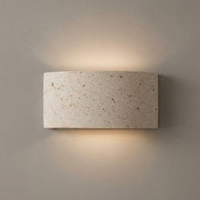 Compact rectangular travertine up/down wall light casting warm glow on a neutral wall.