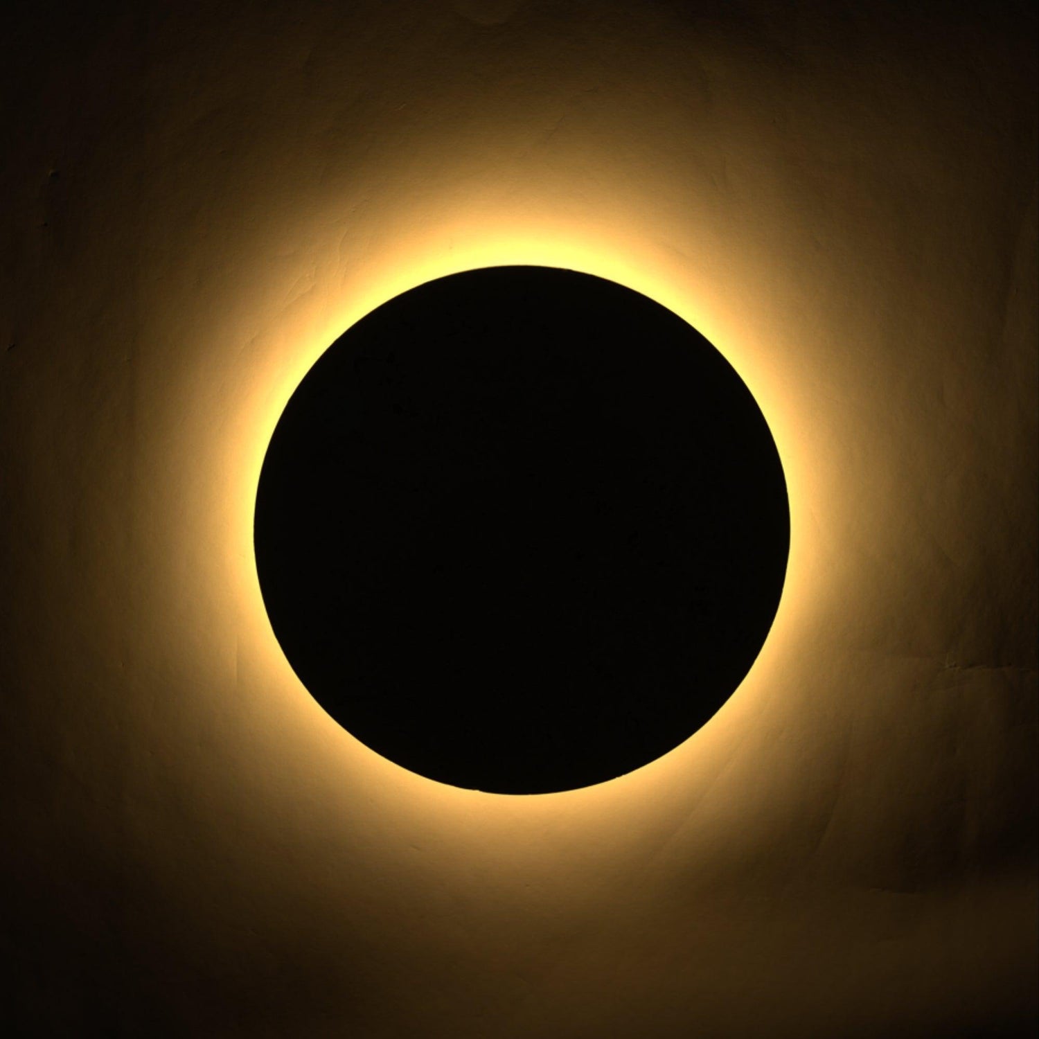 Shore Travertine Halo Wall Light: a circular black form with a warm, glowing halo of light.