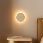 Shore Travertine Halo Wall Light: round, textured beige travertine light with a soft glow on a wall.
