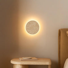 Shore Travertine Halo Wall Light: round, textured beige travertine light with a soft glow on a wall.
